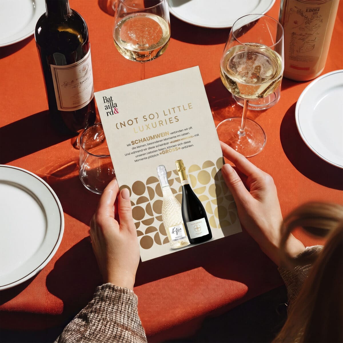 flyer «(not so) little luxuries» für schaumwein in den händen einer person am gedeckten tisch