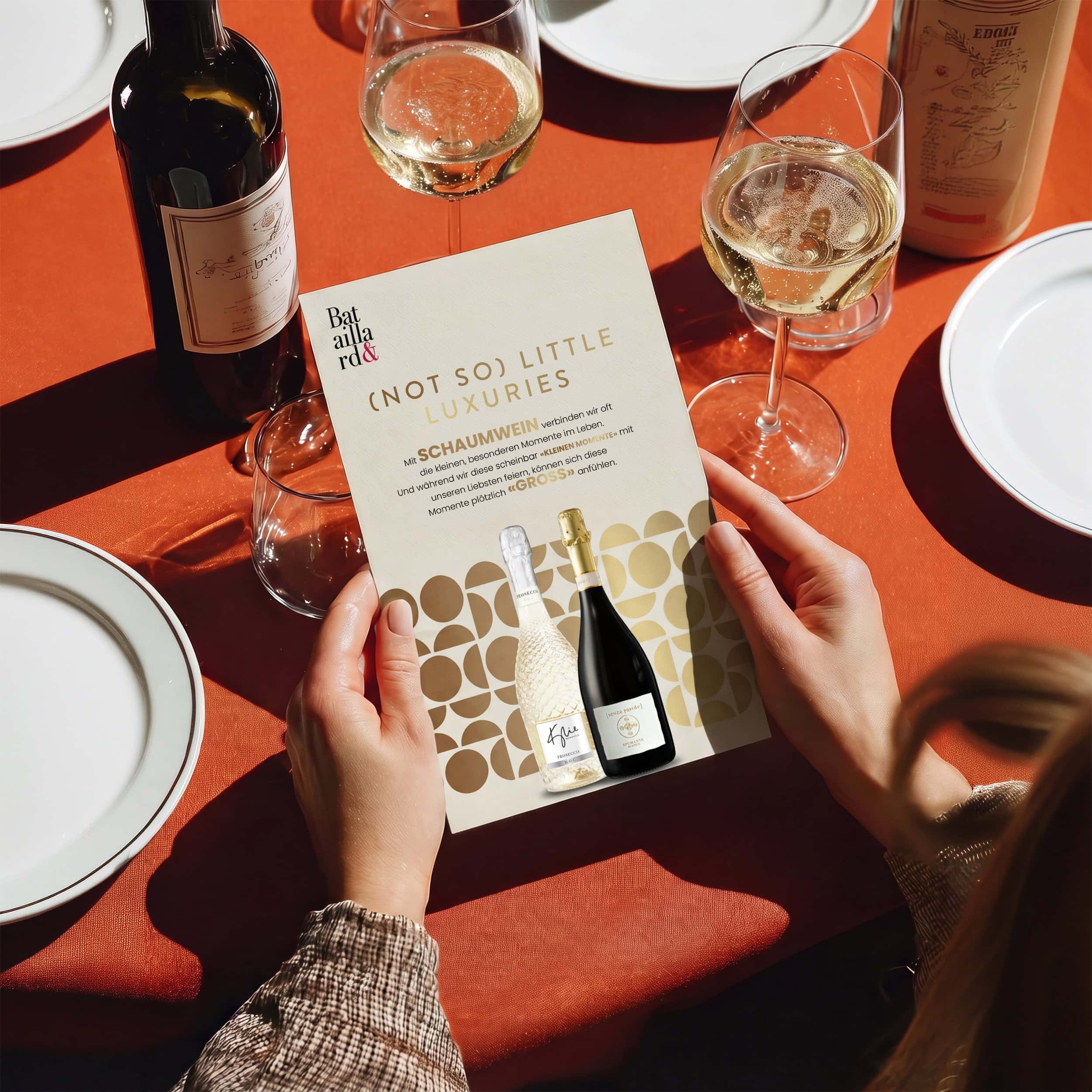 flyer «(not so) little luxuries» für schaumwein in den händen einer person am gedeckten tisch