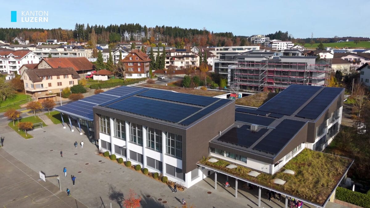luftaufnahme eines schulhauses mit solardach in einem dorf