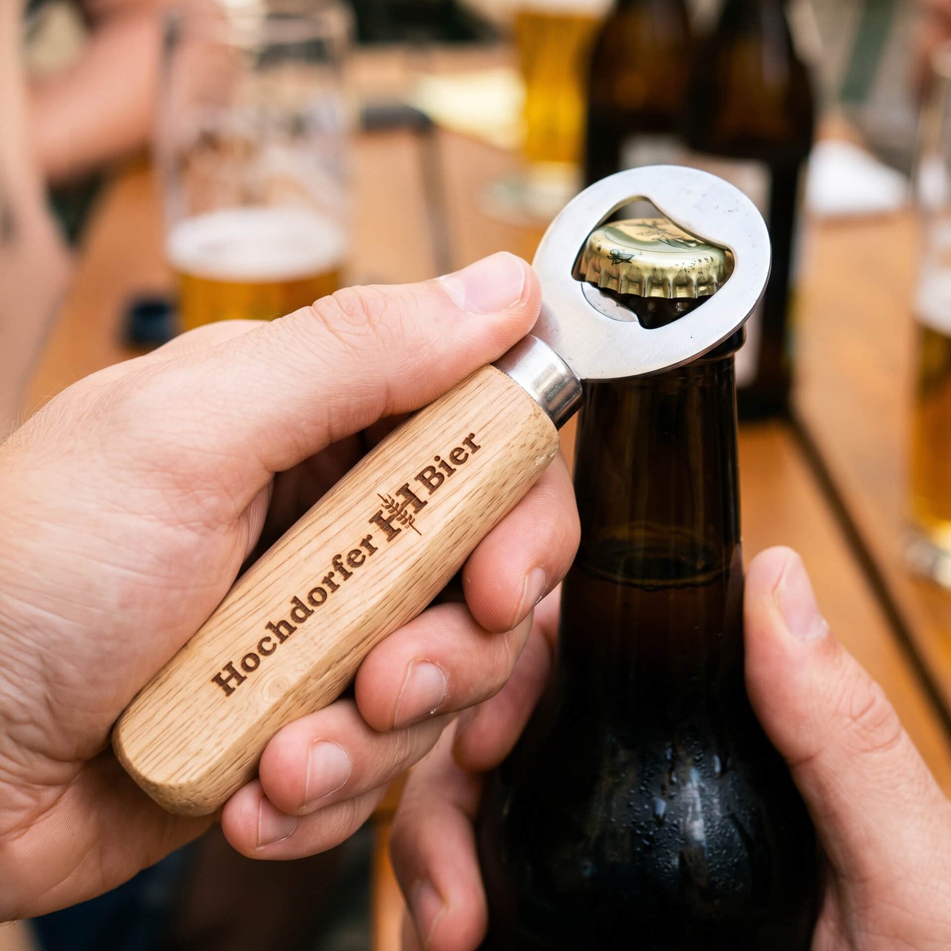 flaschenöffner aus holz mit hochdorfer-bier-gravur beim öffnen einer flasche