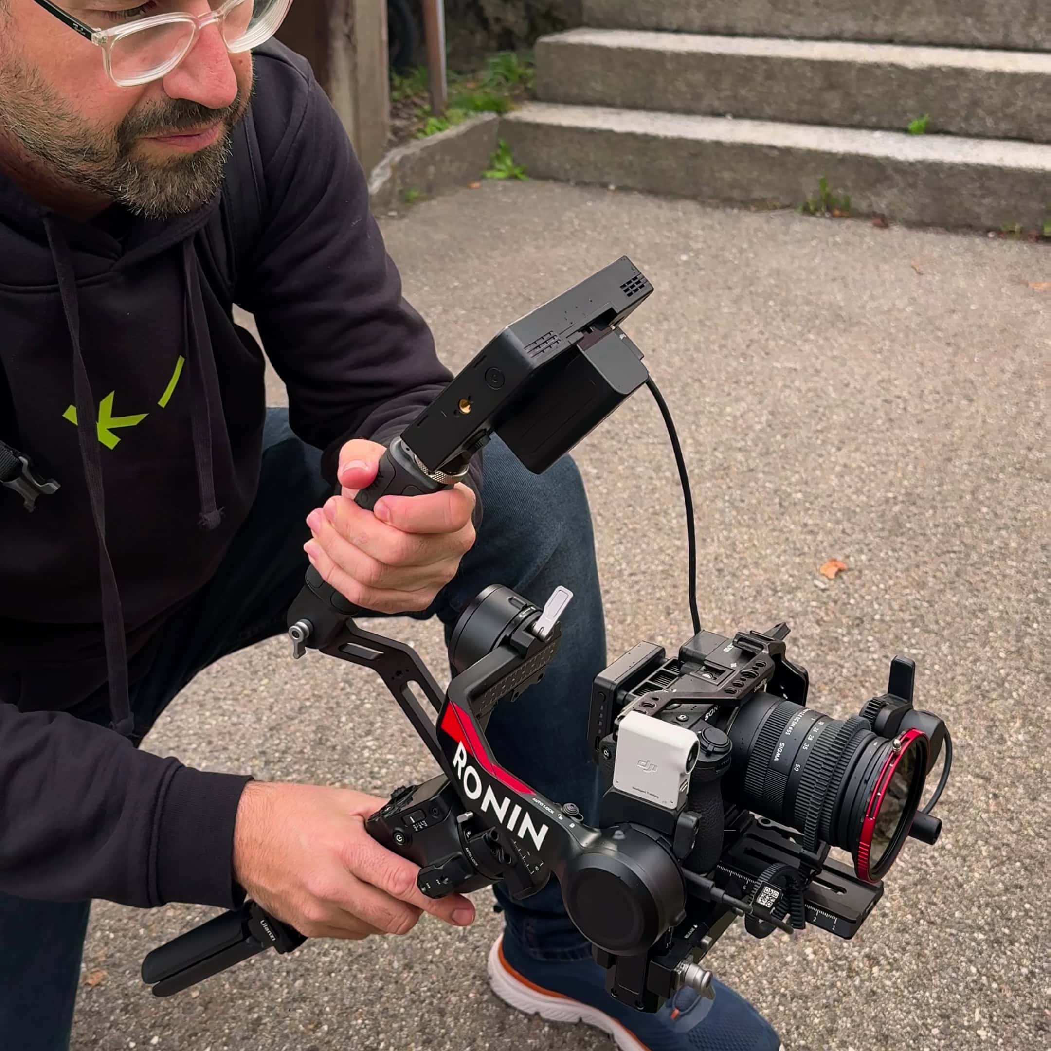 videograf mit gimbal-kamera kniet auf einem platz vor einer treppe