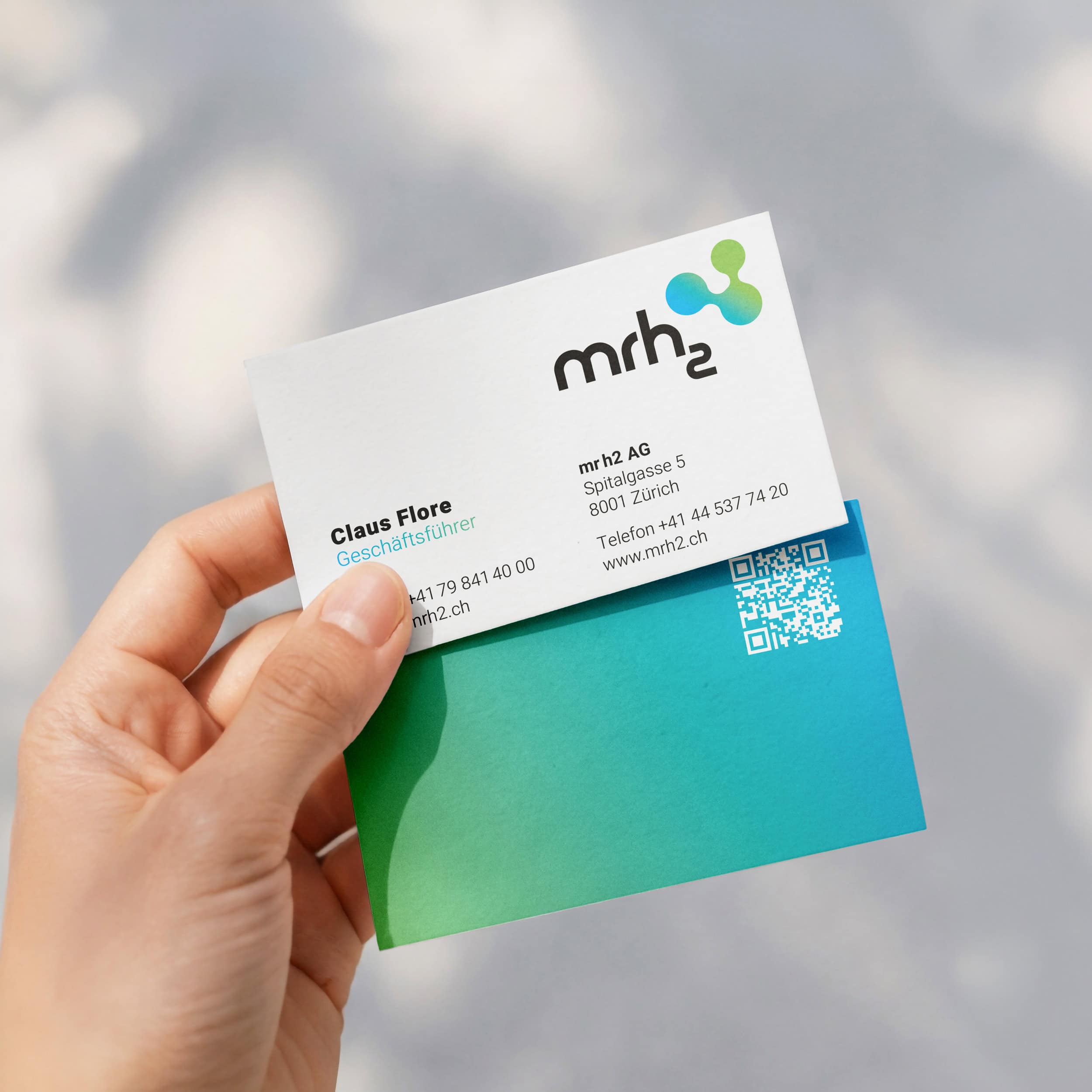 hand hält eine visitenkarte von mrh2 mit logo und farbverlauf von blau zu grün