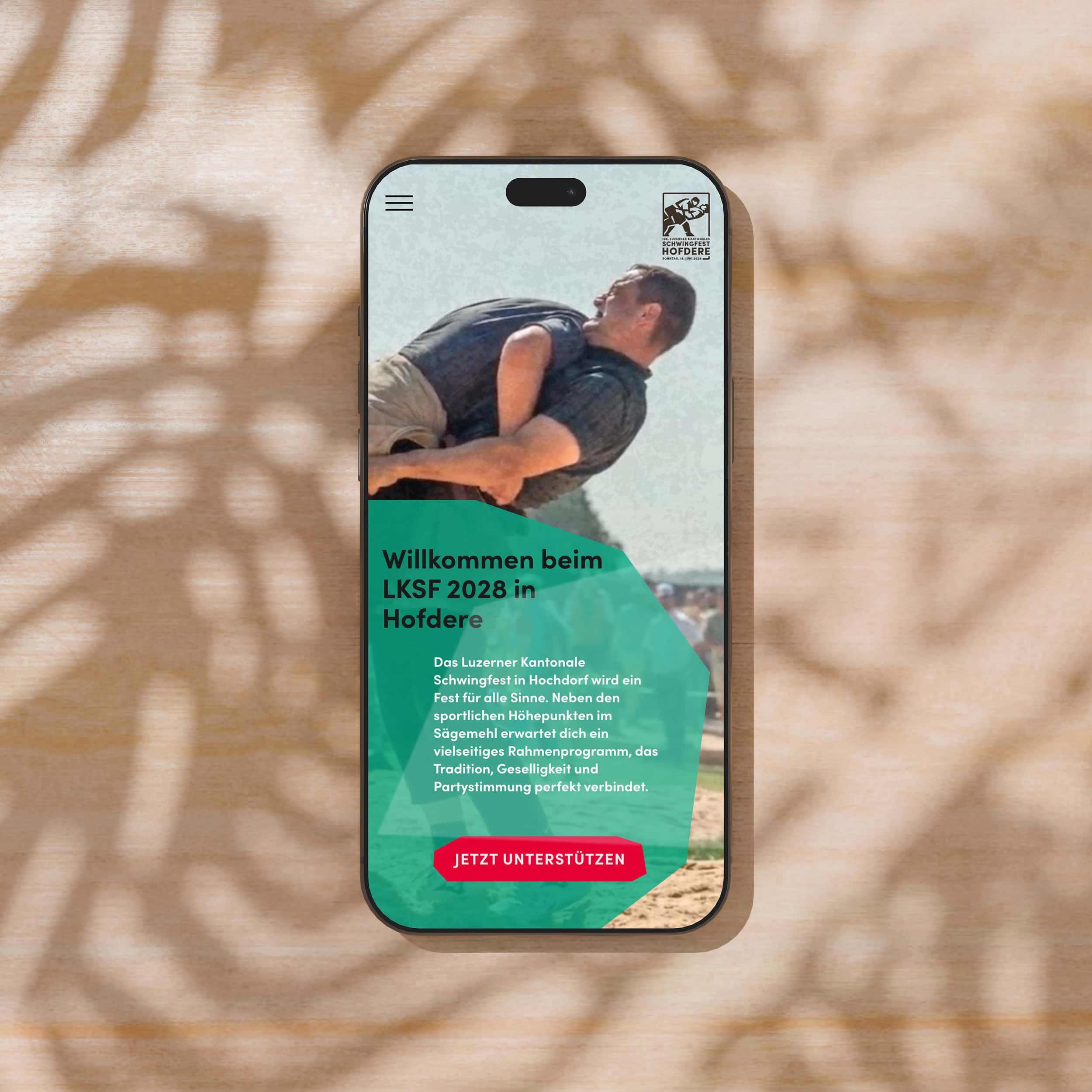 smartphone mit der startseite der website des schwingfests hofdere vor blattschatten